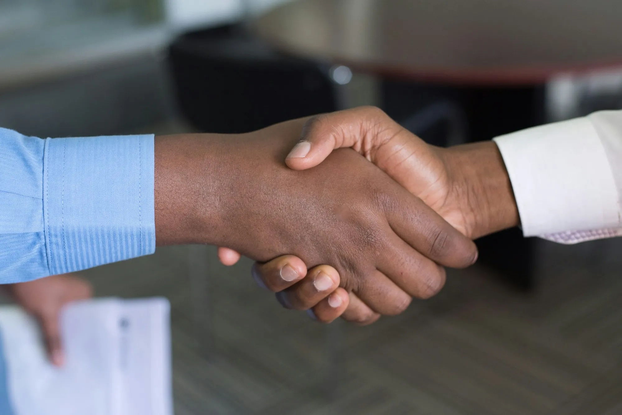 Two professionals shaking hands across a meeting room.