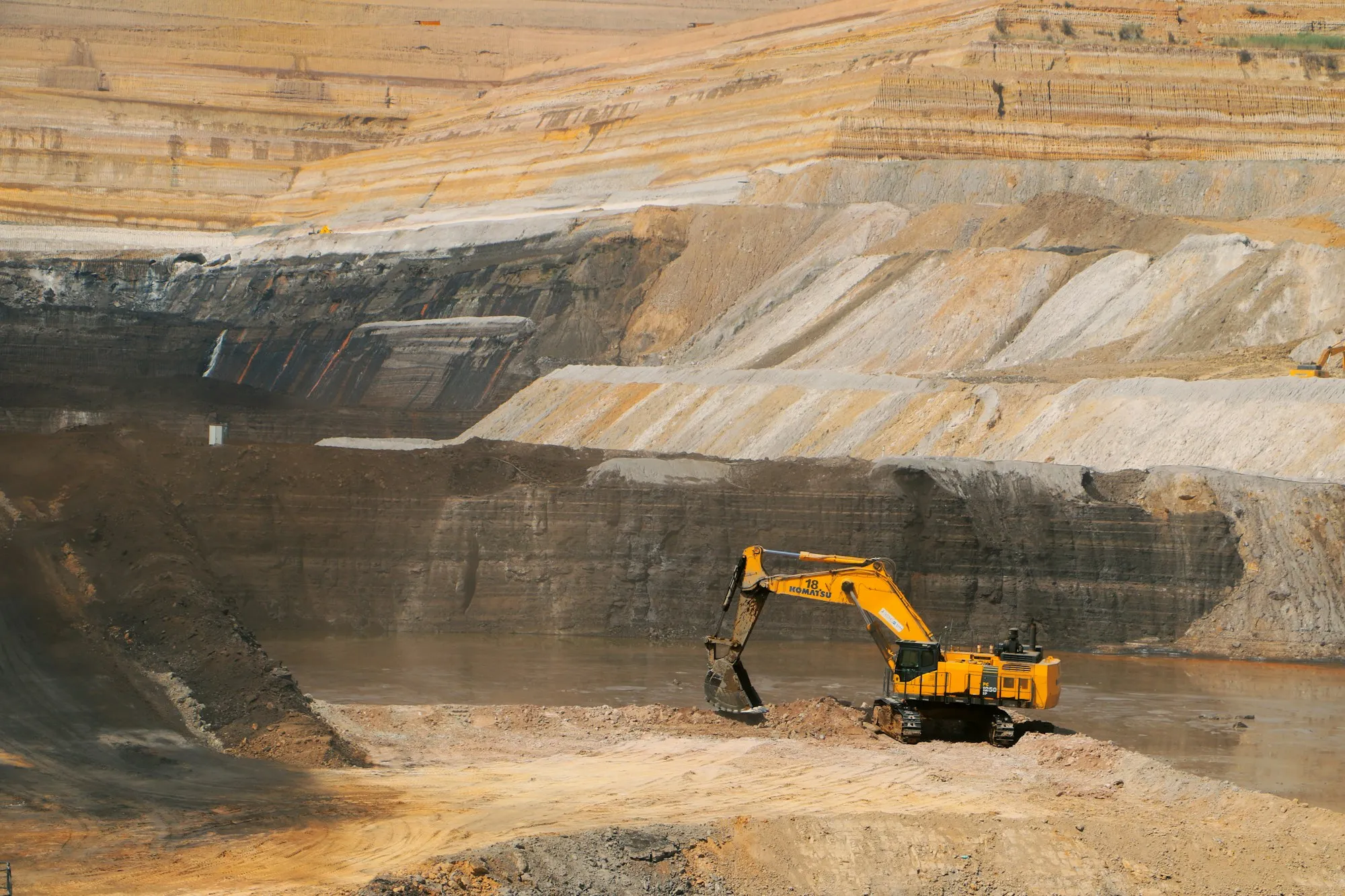 Yellow excavator working in a layered open-pit gold mine.